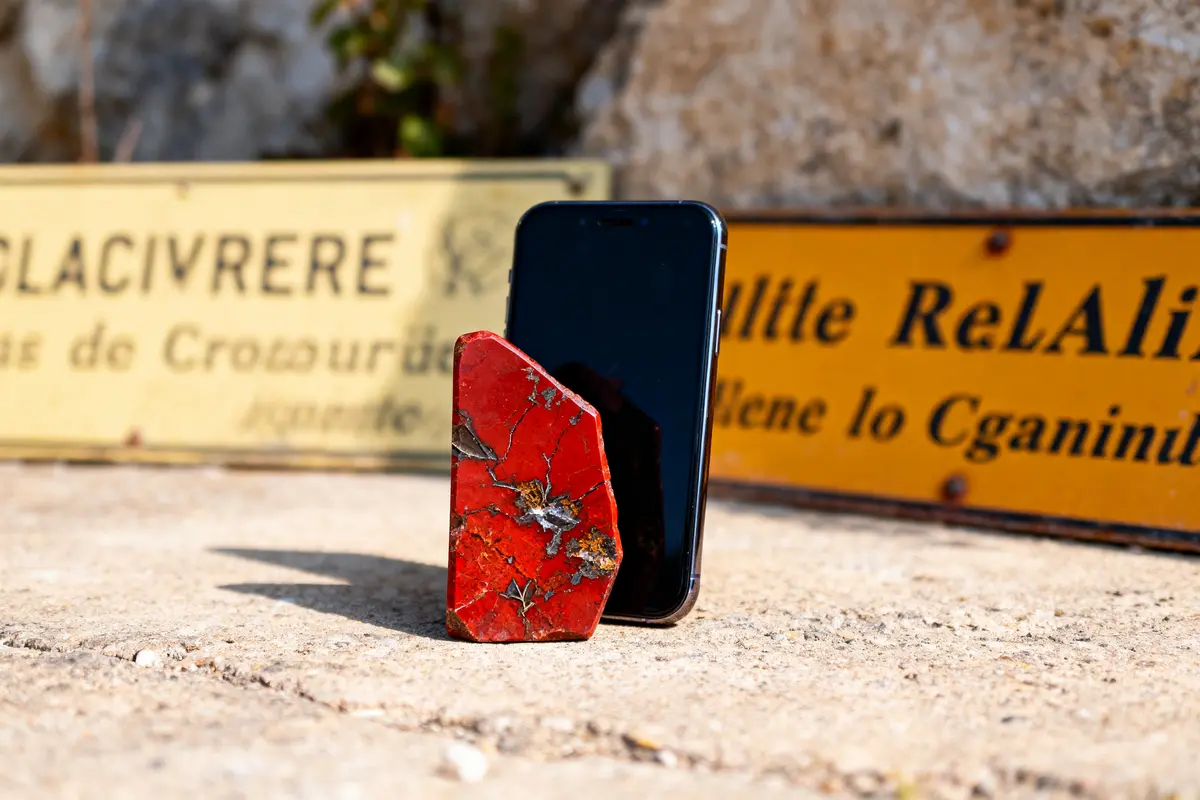 Pierre rouge et smartphone posés sur sol en béton, panneaux flous en arrière-plan.