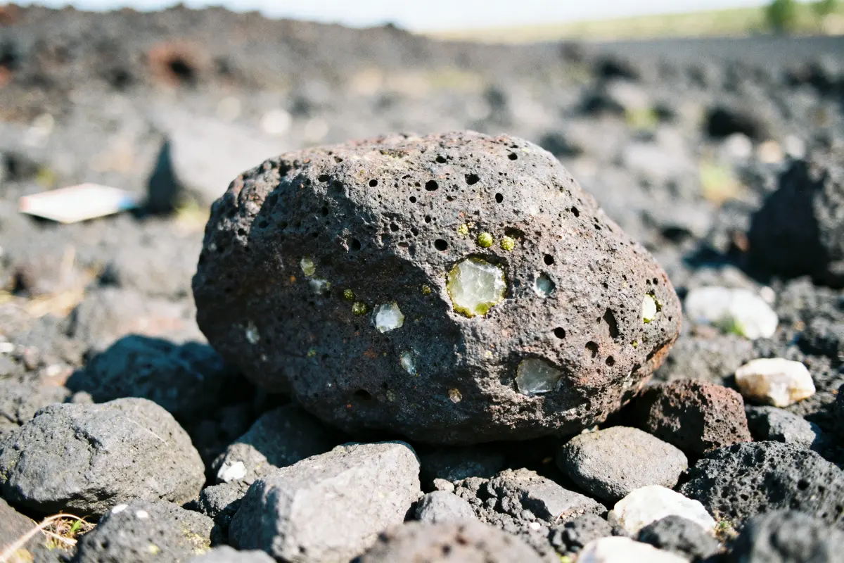 Gros plan de roche volcanique avec cristaux verts et blancs, posée sur sol rocheux.