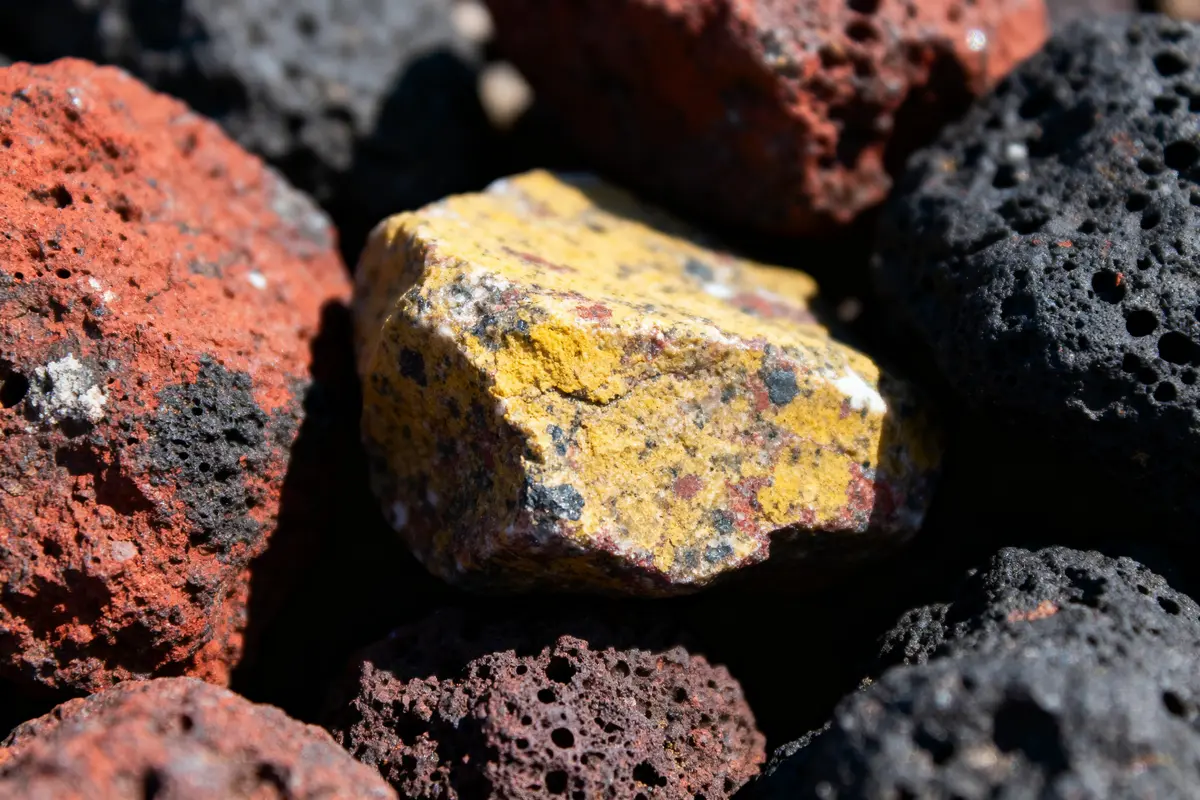 Roches volcaniques rouges, noires et jaunes avec surface poreuse et texture rugueuse, éclairées par le soleil.
