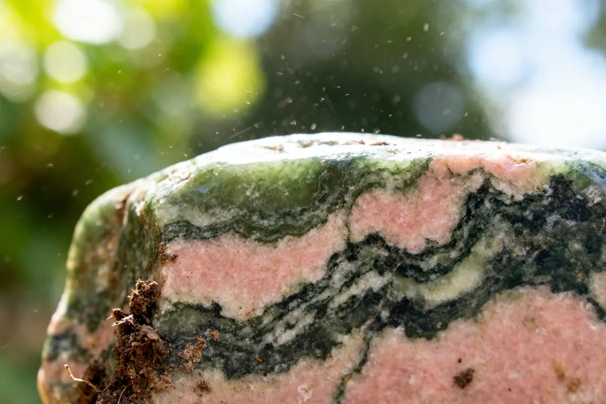 Gros plan d'une pierre avec des motifs verts et roses, lumière naturelle en arrière-plan.