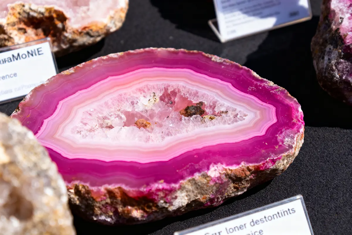 Géode d'améthyste rose coupée, avec couches concentriques et cristaux au centre, exposée sur fond noir.