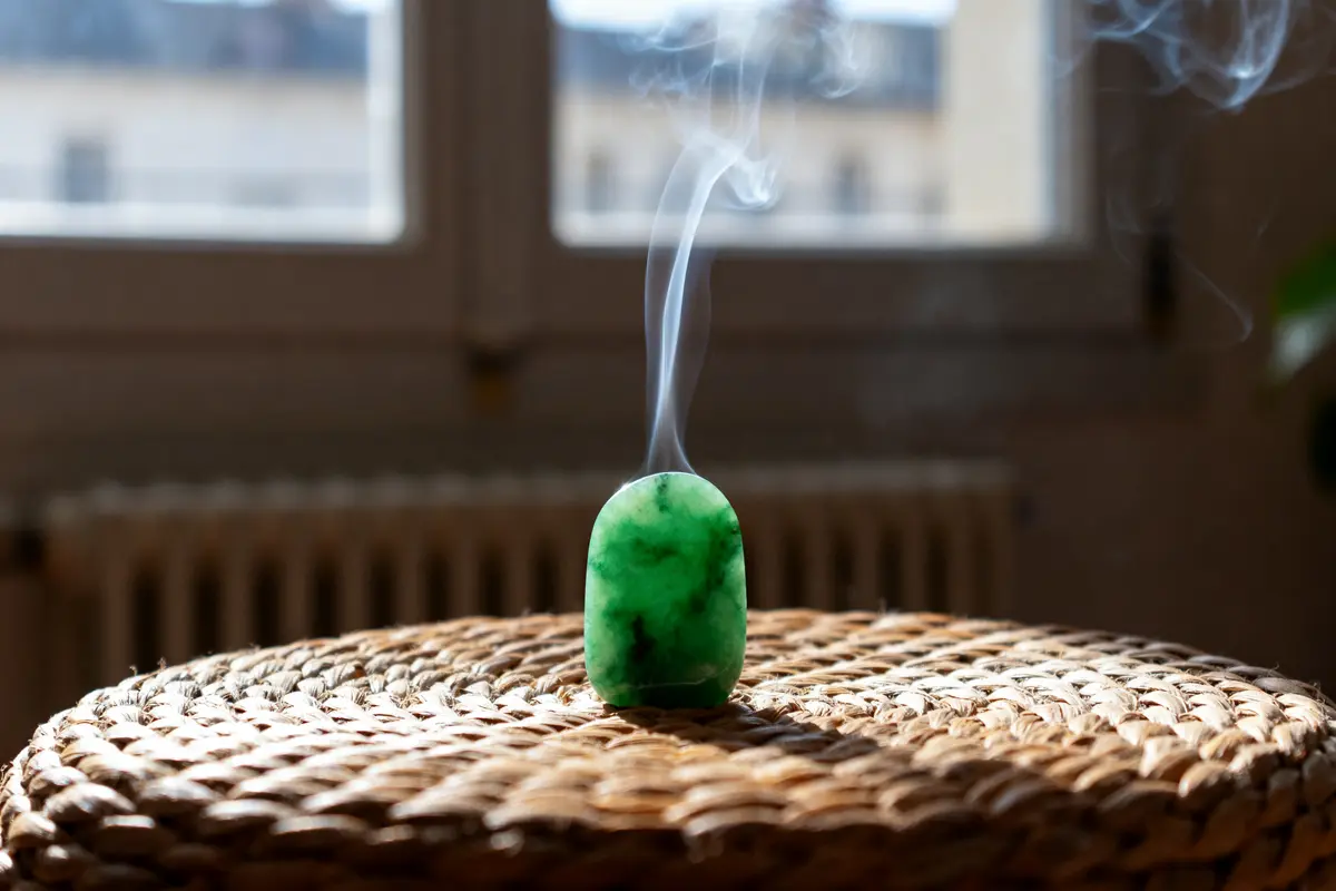 Bougie verte fumante sur une table en osier, lumière naturelle entrant par la fenêtre en arrière-plan.