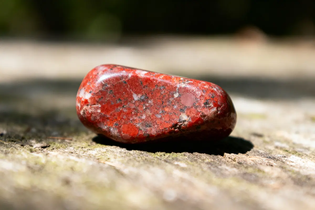 Galet rouge brillant, posé sur une surface texturée, éclairé par la lumière naturelle.