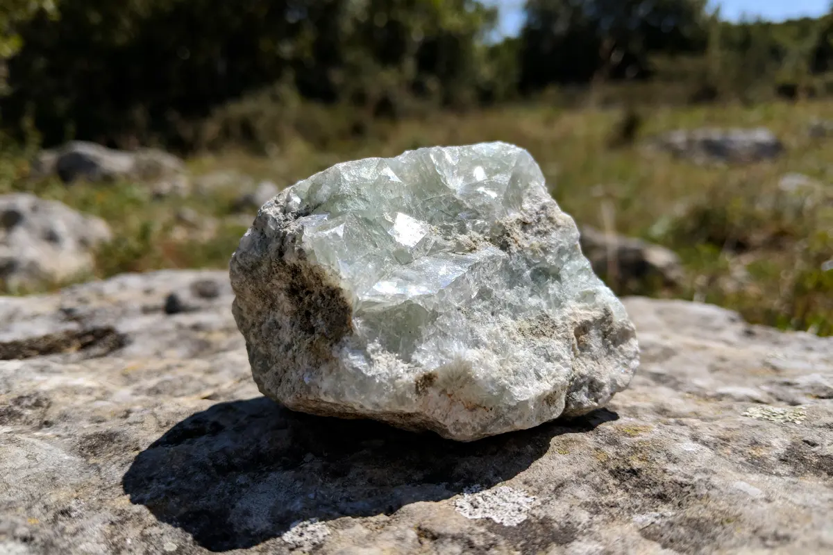 Roche cristalline translucide sur fond de nature floue, éclairée par le soleil, posée sur pierre grise.