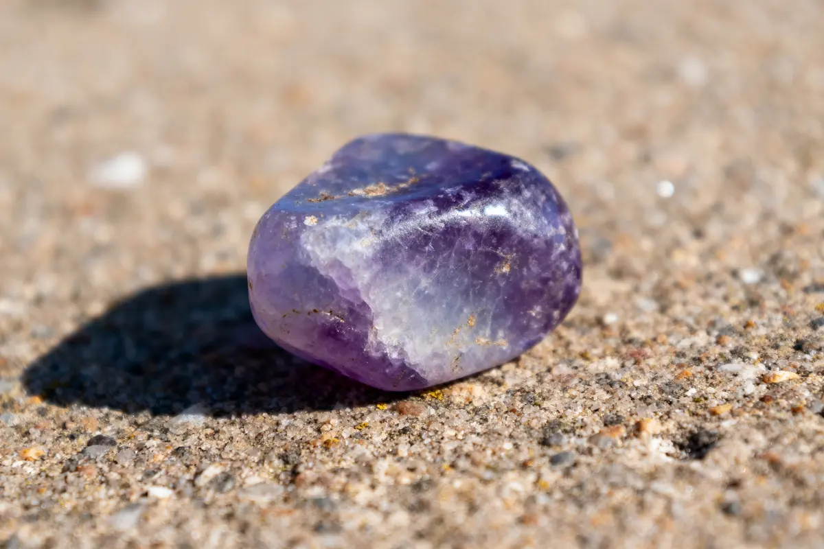 Pierre violette polie sur sol granuleux en gros plan, avec éclairage naturel.