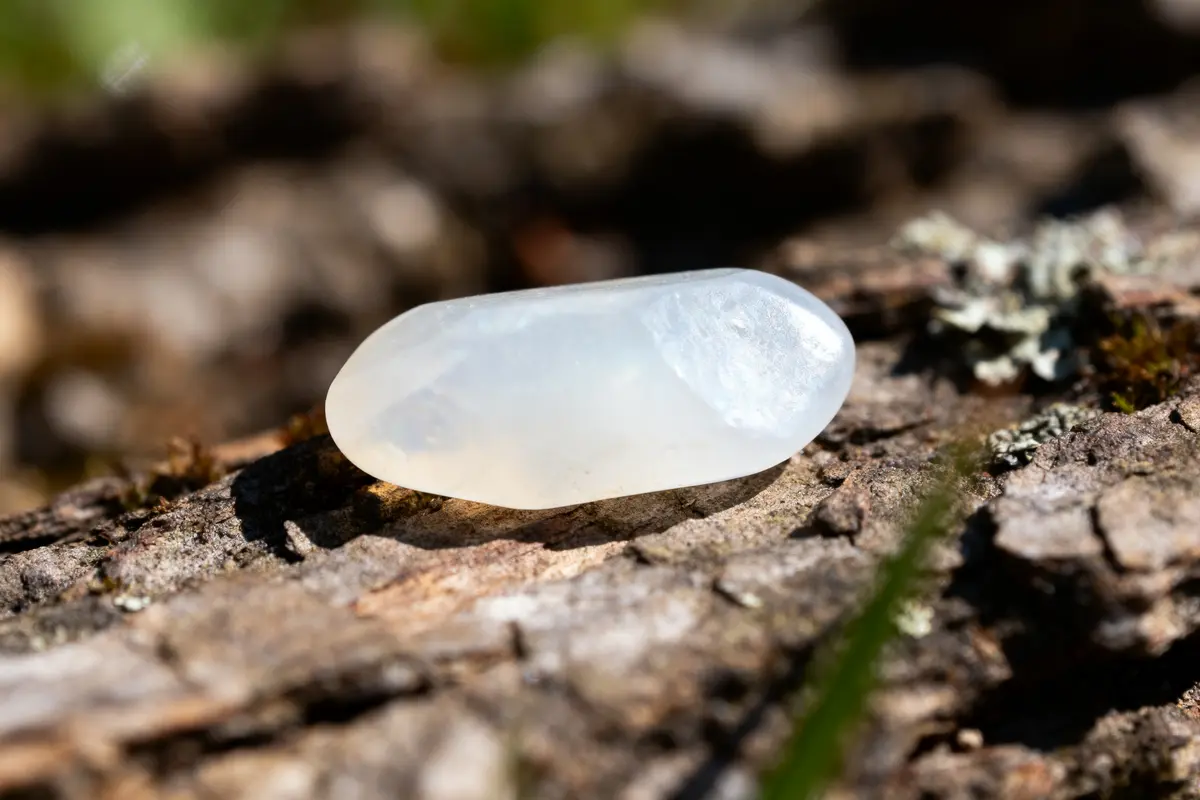 Pierre translucide et polie posée sur une surface rugueuse en bois, éclairée par le soleil.
