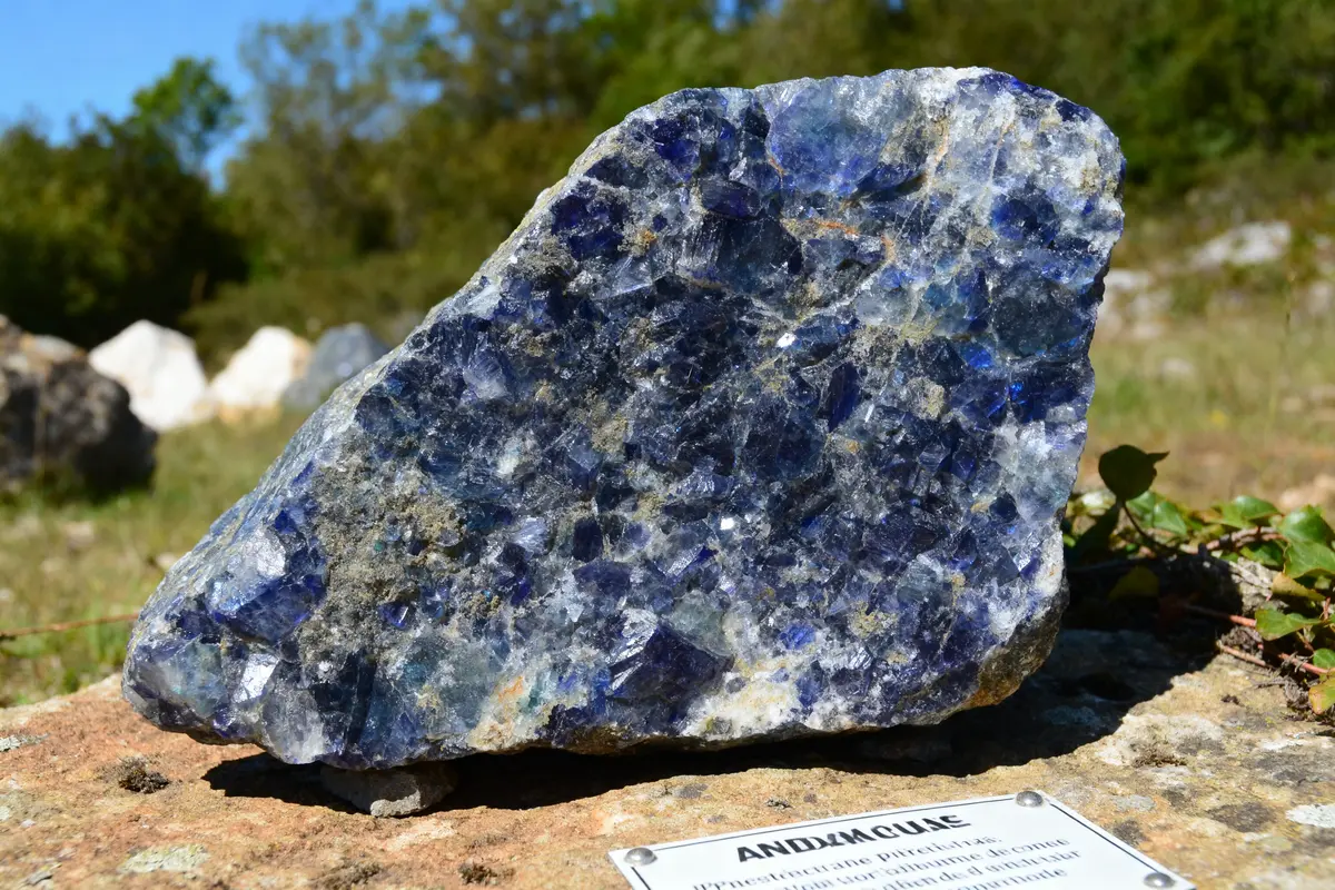 Gros plan d'une roche bleue et grise avec inscription "ANDESMOUSE" en extérieur, végétation floue en arrière-plan.