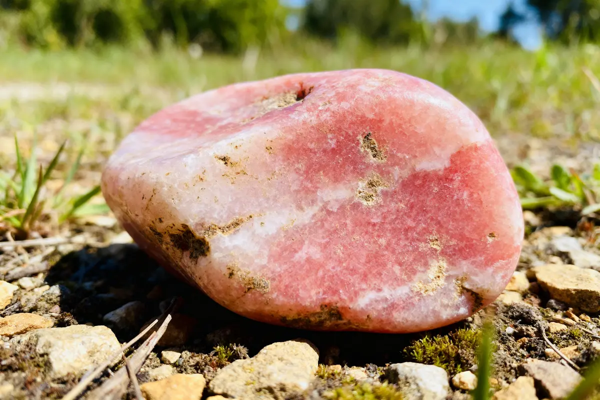 Pierre de rhodochrosite rose sur sol rocheux illustrant les vertus de la rhodochrosite